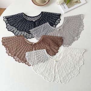Op de afbeelding: Vijf kanten kragen in verschillende kleuren: zwart, grijs, bruin en wit. Elke kraag heeft een geschulpte rand en een delicaat stippenpatroon. Een kleine parelknop sluit elke kraag en biedt een vintage esthetiek.