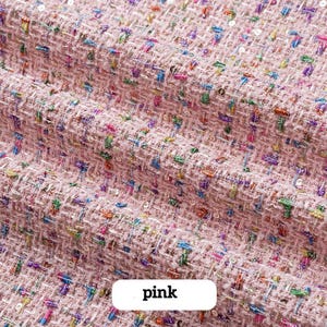 Könnte beinhalten: Nahaufnahme eines rosa Tweed-Stoffs mit bunten Flecken und dezenten Pailletten. Der Stoff hat eine gewebte Textur und das Wort "pink" wird in einem weißen Rechteck angezeigt.