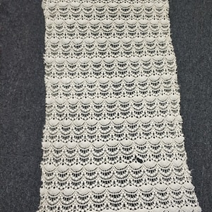 May include: White crocheted fabric with a scalloped pattern. The fabric is delicate and has a soft texture.