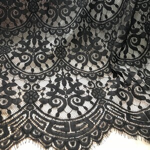 Puede incluir: Tela de encaje negra con un delicado patr&oacute;n floral. El encaje tiene un borde festoneado y una textura ligeramente deshilachada.