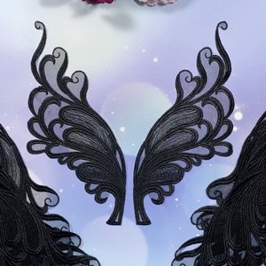 Puede incluir: Tres aplicaciones de encaje negro en forma de alas. Las alas están detalladas con intrincados remolinos y curvas.