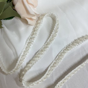 May include: White beaded trim with a delicate, swirling pattern. The trim is made of small, white beads sewn onto a white fabric base.