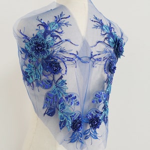 Könnte beinhalten: Blaue Blumenapplikation mit Pailletten und Perlen auf einem durchsichtigen Netzstoff.