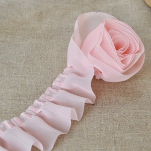 Può includere: Frange rosa arricciata con un dettaglio a forma di rosa assemblata. Questo bordo è perfetto per aggiungere un tocco di eleganza a qualsiasi progetto.
