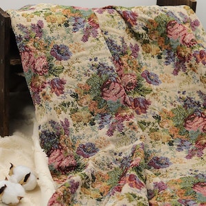 Könnte beinhalten: Ein beiger floraler Gobelinstoff mit einem detaillierten Muster aus Rosen, anderen Blumen und Blättern in Rosa-, Lila-, Blau-, Grün- und Orangetönen. Der Stoff ist über einer Holzstruktur drapiert, mit Baumwollkugeln im Vordergrund.