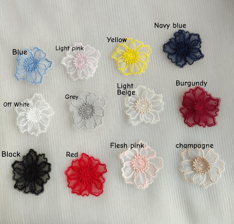 May include: A collection of twelve embroidered flower appliques in various colors including blue, light pink, yellow, navy blue, off white, grey, light beige, burgundy, black, red, flesh pink, and champagne, each labeled with its color name.
