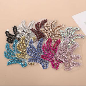 May include: A collection of rhinestone leaf appliques in various colors, including black, silver, burgundy, gold, teal, yellow, blue, fuchsia, and pink. Each applique is made of small, sparkling rhinestones arranged in a leaf shape.