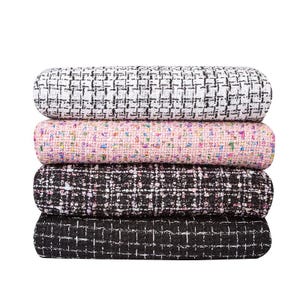 May include: Four rolls of fabric in a stack. The top roll is white and black, the second is pink with colorful flecks, the third is black and white, and the bottom is black. The fabric has a woven tweed texture.