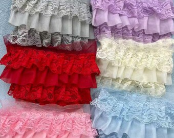 Può includere: Assortimento di bordi in pizzo a balze in vari colori, tra cui grigio, rosso, rosa, viola, giallo e blu. Il pizzo presenta un delicato motivo floreale ed è stratificato con un tessuto trasparente, creando un effetto strutturato e voluminoso.