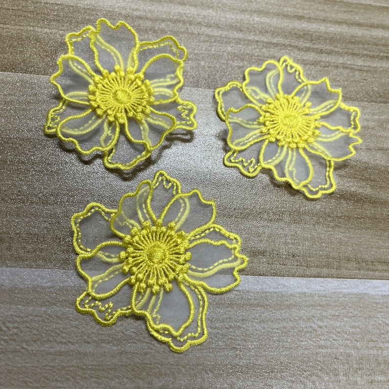 May include: Three flower-shaped appliques featuring bright yellow embroidery thread outlining translucent white organza petals. Each piece has a dense, circular yellow embroidered center with radiating lines, creating a delicate floral design.
