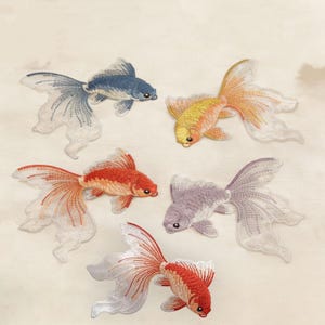Puede incluir: Cinco parches bordados de peces dorados con un intrincado trabajo de hilo. La colección incluye un pez azul, uno amarillo y naranja, uno naranja brillante, uno morado claro y uno rojo y blanco, todos con aletas y colas muy detalladas.
