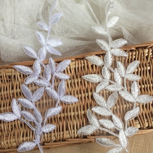 May include: Two white lace appliques in the shape of leafy branches. The appliques are on a woven wicker surface.