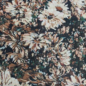 May include: A woven fabric featuring a dense floral pattern of large, cream-colored daisy-like flowers against a dark background. The design incorporates shades of brown, tan, and subtle hints of green, creating a textured, multi-layered appearance.