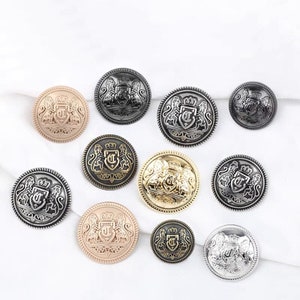 Puede incluir: Surtido de diez botones metálicos decorativos con un escudo con una corona y dos leones. Los botones están disponibles en varios acabados, incluyendo oro, plata, negro y oro rosa.