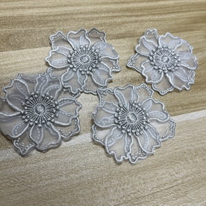 May include: Four individual flower-shaped appliques featuring sheer white organza petals with intricate silver metallic embroidery outlining the edges and a dense, textured silver thread center. Each piece displays a delicate, layered floral design.