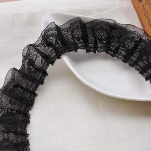 May include: Black lace trim with a ruffled design. The lace has a floral pattern.