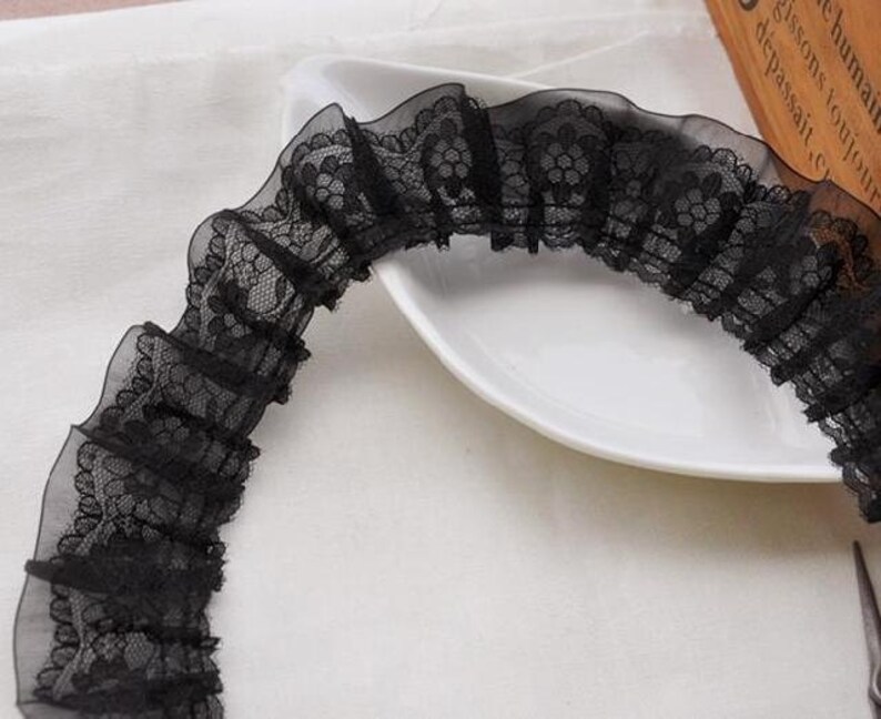 May include: Black lace trim with a ruffled design. The lace has a floral pattern.