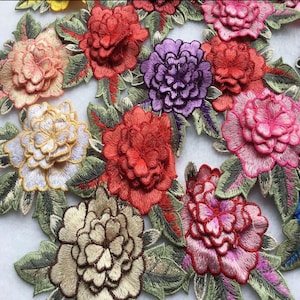 May include: Close-up of embroidered floral appliques in various colors. The flowers include shades of red, pink, purple, and gold, with green leaves. The embroidery has a 3D effect, creating a textured appearance. These appliques are suitable for fabric crafts.