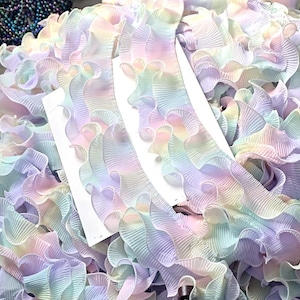 Może przedstawiać: Pastelowa falbanka w kolorach tęczy. Ozdoba ma falisty, plisowany wzór z miękkimi odcieniami różu, błękitu, żółci i zieleni. Ta dekoracyjna ozdoba jest idealna do szycia i rękodzieła.