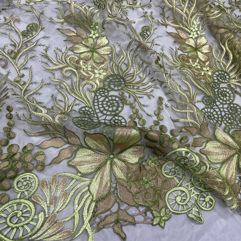 K&ouml;nnte beinhalten: Gr&uuml;ne und goldene florale Stickerei auf einem durchsichtigen Stoff. Das Design zeigt komplizierte Wirbel und zarte Blumen.