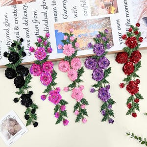 May include: Five vertical floral appliques featuring sequined petals and green embroidered leaves. The set includes one black, one magenta, one light pink, one purple, and one red floral arrangement, each with a long, slender stem design.