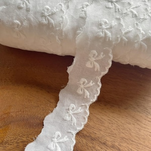 Peut inclure: Galon de dentelle en coton blanc avec un bord festonné et des nœuds brodés.