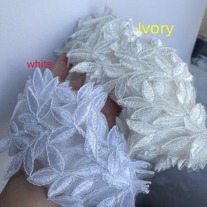 May include: Two swatches of lace fabric, one white and one ivory, with a leaf pattern. The fabric is delicate and has a soft, flowing texture.
