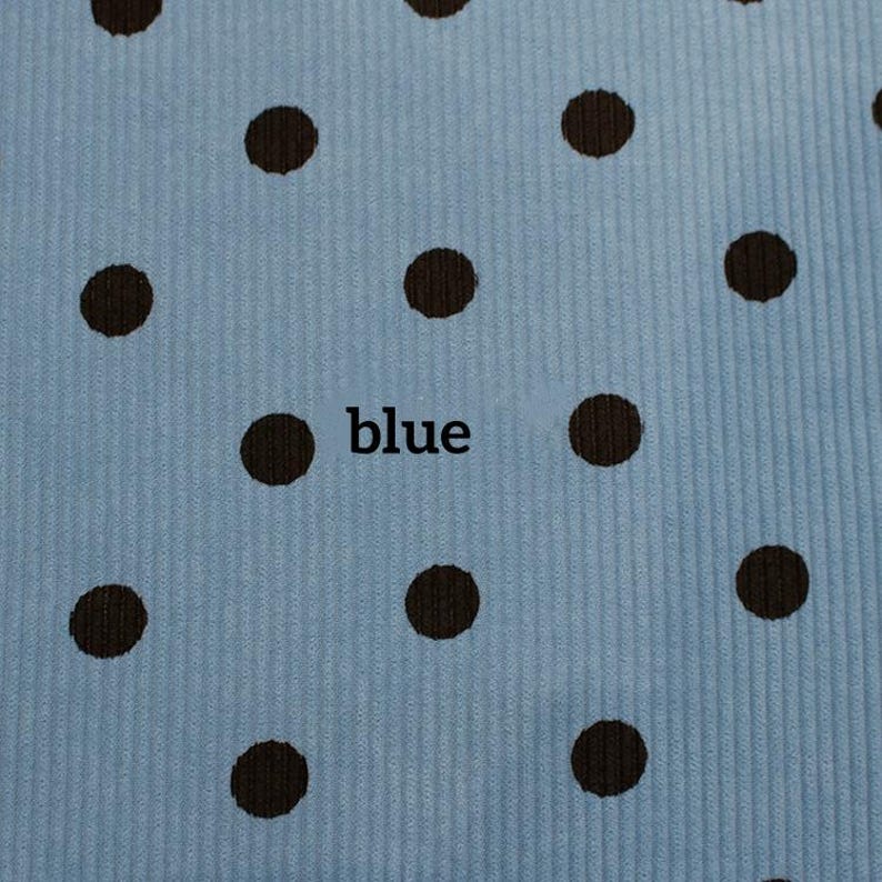 May include: A light blue fabric with a vertical ribbed texture and a repeating pattern of dark brown polka dots. The word blue is printed in black lowercase letters in the center of the fabric, positioned between two of the brown dots.