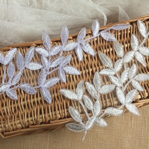 May include: Two silver leaf lace appliques with a delicate floral design. The appliques are on a woven wicker surface.