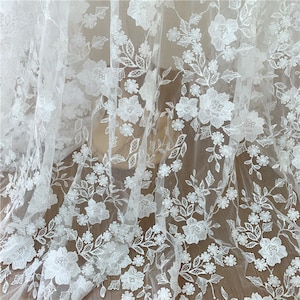 Puede incluir: Tela de encaje floral blanco con flores y hojas bordadas. El material transparente es ideal para vestidos de novia, vestidos o proyectos decorativos. El intrincado dise&ntilde;o muestra una variedad de patrones florales, creando una est&eacute;tica rom&aacute;ntica y elegante.