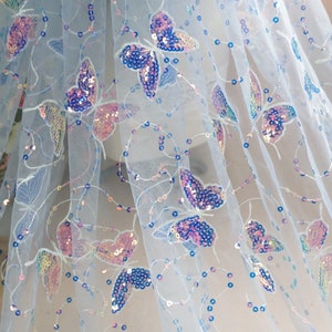 May include: White sheer fabric with iridescent butterfly sequins. The fabric has a delicate, airy feel and is perfect for adding a touch of sparkle to any project.