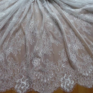 Tecido de renda floral off-white com detalhes em margaridas e borda ondulada, ideal para vestidos de noiva, mantilhas e vestidos de festa/pijama. Vendido por 1 jarda.