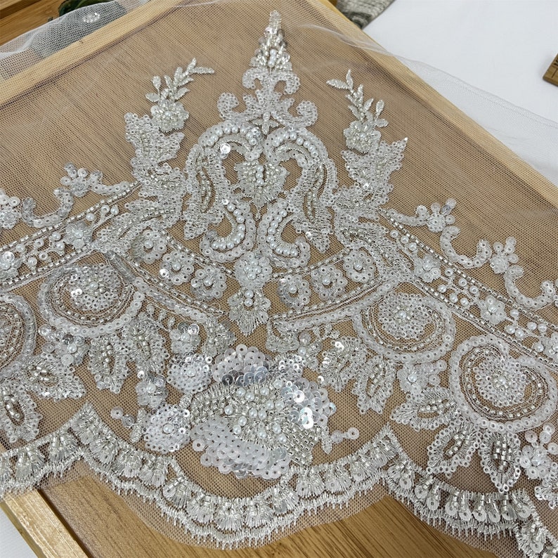 Pu&ograve; includere: Bordino di pizzo bianco perlato e paillettes con un bordo smerlato. Il bordino presenta un motivo floreale con un motivo di tipo paisley.