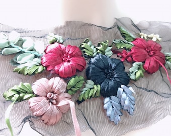 May include: A black mesh fabric with a floral design made of colourful ribbon. The flowers are pink, red, blue, and green.