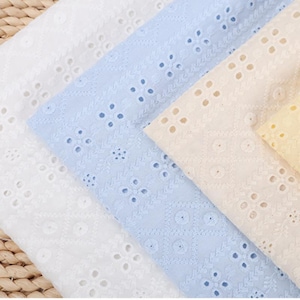 Puede incluir: Una colección de muestras de tela bordada en blanco, azul claro, crema y amarillo pálido. Cada pieza de tela presenta un patrón geométrico repetitivo de recortes circulares bordados y delicados motivos florales dispuestos en filas diagonales.
