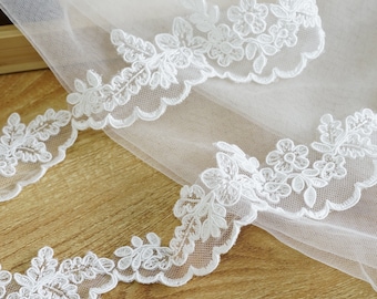 May include: White lace trim with a scalloped edge and floral designs. The lace is delicate and intricate, with small flowers and leaves.