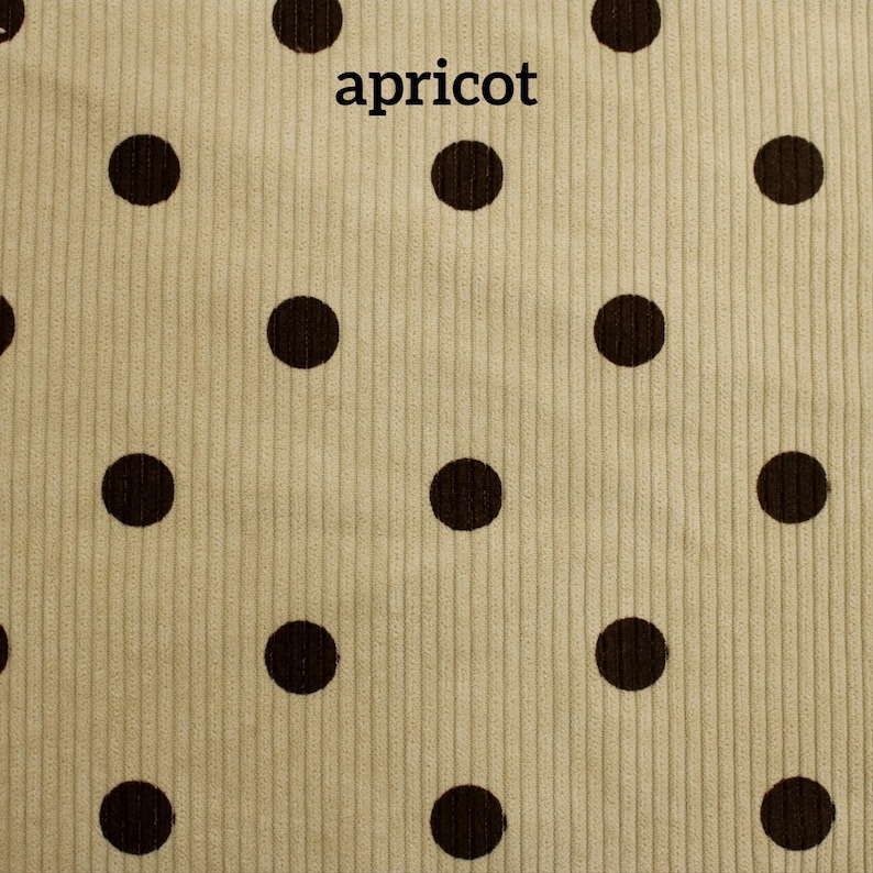 May include: A light beige corduroy fabric featuring a repeating pattern of dark brown polka dots. The word apricot is printed in black lowercase letters near the top center of the textile, which has a distinct vertical ribbed texture.