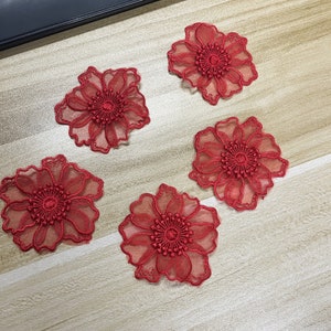 May include: Four individual red flower appliques featuring sheer, translucent petals with intricate, dense embroidery detailing at the center. Each floral piece has a scalloped edge and a layered, delicate construction for textile projects.