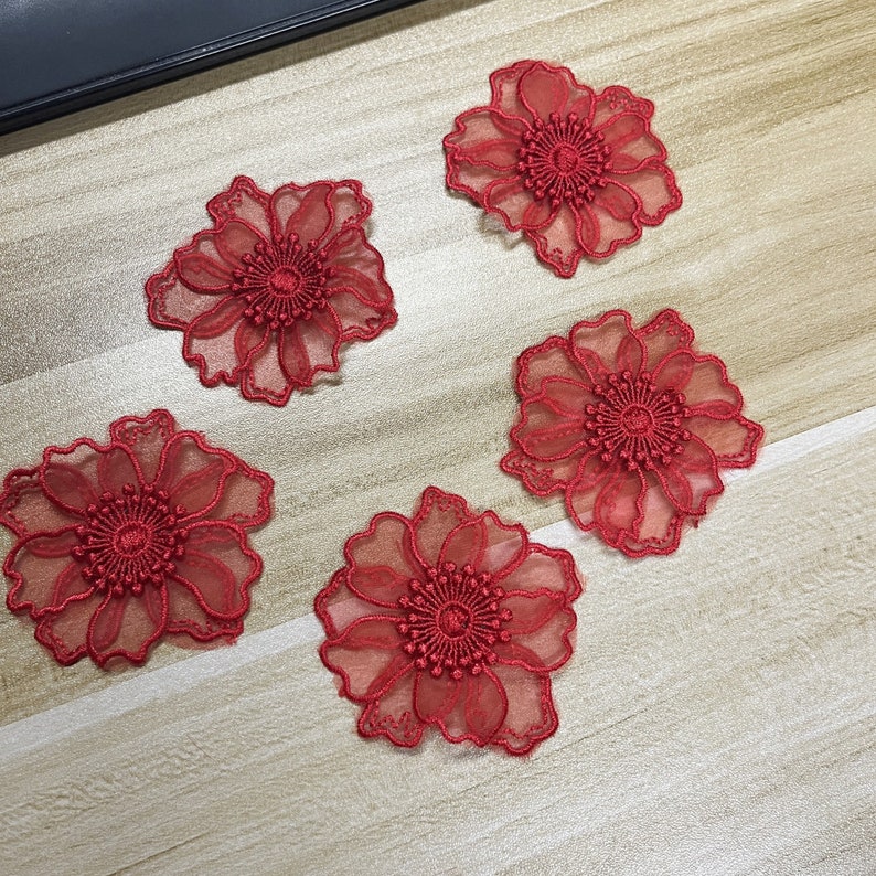 May include: Four individual red flower appliques featuring sheer, translucent petals with intricate, dense embroidery detailing at the center. Each floral piece has a scalloped edge and a layered, delicate construction for textile projects.