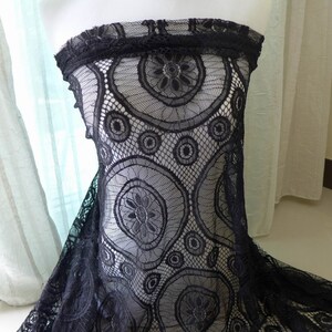 Peut inclure: Un tissu en dentelle noire pr&eacute;sentant un motif r&eacute;p&eacute;titif de grands et petits cercles avec des centres floraux complexes. Le mat&eacute;riau poss&egrave;de une structure en maille semi-transparente avec un bord festonn&eacute; sur la partie sup&eacute;rieure.