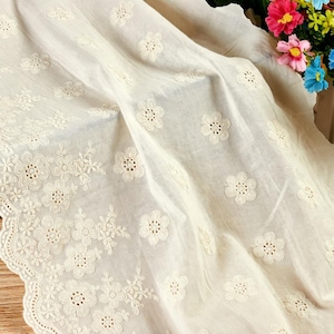 Peut inclure: Un tissu blanc cassé orné d'un motif floral brodé complexe avec de petites fleurs répétitives. Le matériau présente un bord festonné sur un côté, mettant en valeur un travail d'aiguille détaillé et une texture délicate et légère.