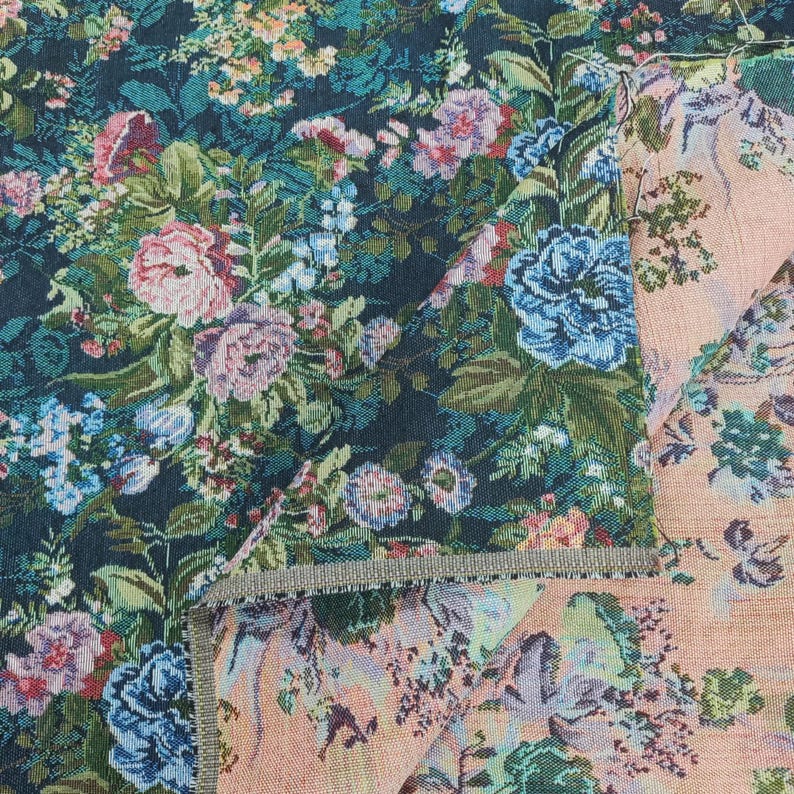 Puede incluir: Una tela tejida con un denso patr&oacute;n floral de flores rosas, azules y blancas sobre un fondo azul marino oscuro. El reverso del tejido muestra una base m&aacute;s clara, de color melocot&oacute;n, con una versi&oacute;n tenue del mismo dise&ntilde;o floral.