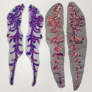 Peut inclure: Quatre appliqués décoratifs avec des motifs floraux à paillettes. Deux présentent des paillettes violettes et bleues, les deux autres roses et dorées. Ils sont sur un support en résille grise.