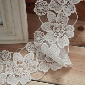 May include: White lace trim with a floral design. The lace is delicate and features a repeating pattern of flowers.