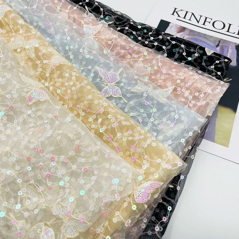 May include: A stack of sheer fabric with butterfly sequins in various colours, including black, pink, beige, light blue, and white.