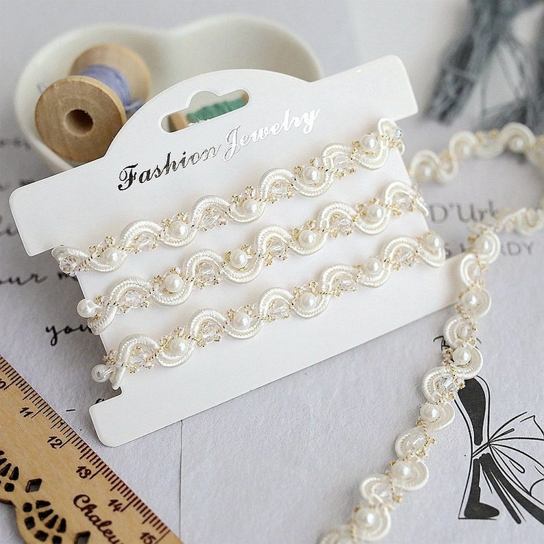 May include: White pearl and gold trim ribbon with the text "Fashion Jewelry" on a white card.