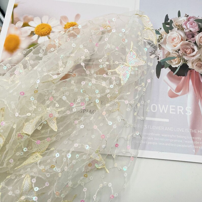 May include: White sheer fabric with iridescent sequins and embroidered butterfly designs. The fabric is delicate and has a soft, flowing texture.