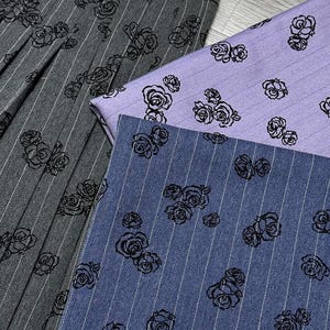 May include: Close-up of three fabrics with a rose pattern. One is gray with white pinstripes, another is a light purple with pinstripes, and the third is blue with pinstripes. All fabrics have a black rose design.