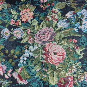 Puede incluir: Una tela tejida que presenta un denso patr&oacute;n floral sobre un fondo negro. El dise&ntilde;o incluye racimos de rosas rosadas, flores azul claro y varias hojas verdes, todo representado con un tejido de hilos texturizado y multicolor.