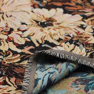 May include: A woven tapestry fabric featuring a dense floral pattern with large cream and beige chrysanthemum-like flowers set against a dark black background. The fabric has a visible textured weave and a frayed edge revealing a blue underside.